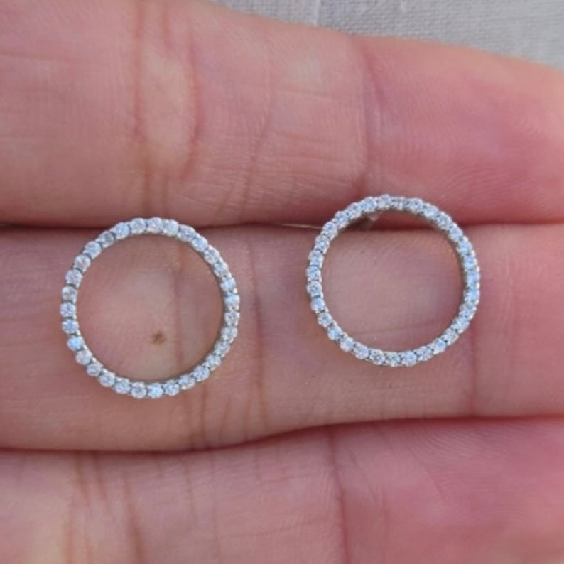 Two diamond earrings held between fingers against a neutral background