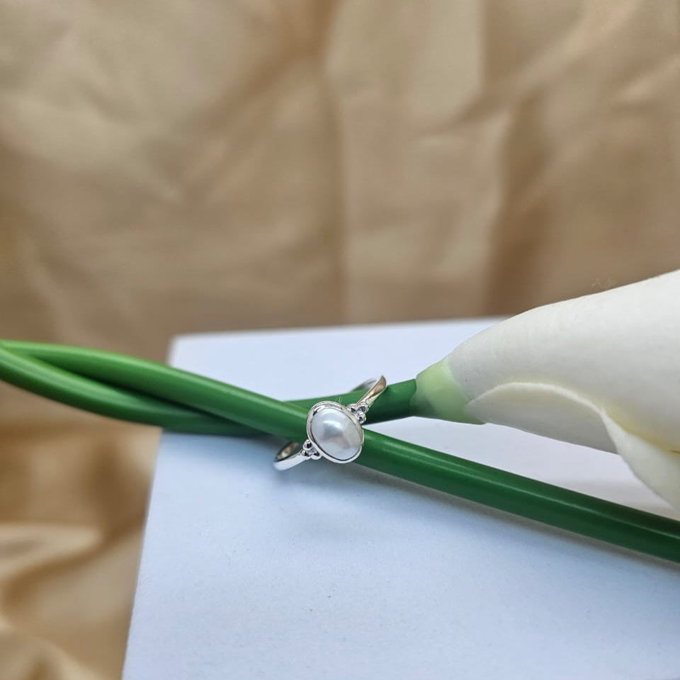 Silver ring with a pearl on a white box with green ribbon and white flowers.