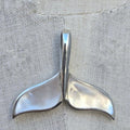 Silver whale tail pendant on a textured fabric background