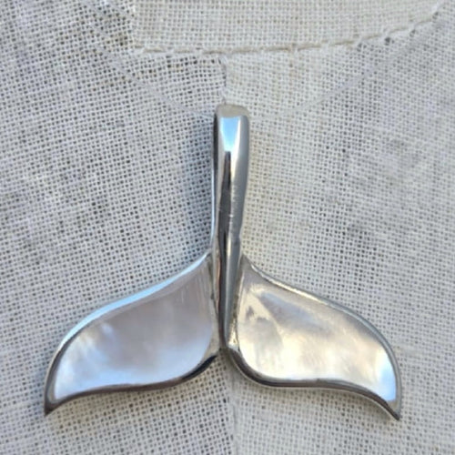 Silver whale tail pendant on a textured fabric background