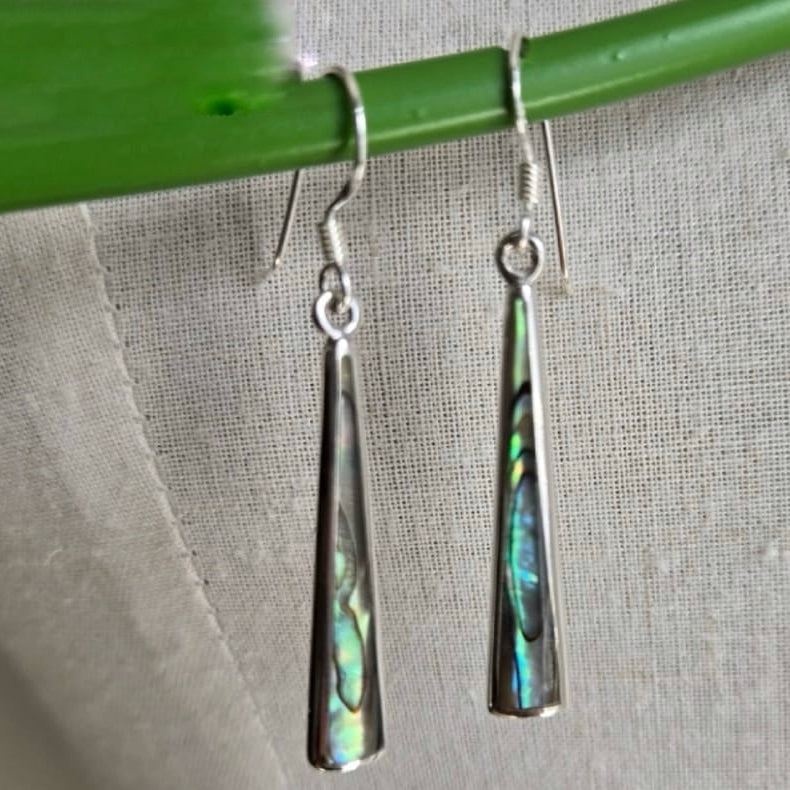 Silver earrings with colorful inlay hanging on a green stick against a gray fabric background