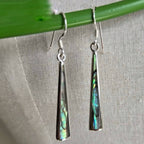Silver earrings with colorful inlay hanging on a green stick against a gray fabric background
