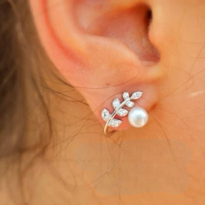 A close-up image of a person's ear wearing a sterling silver hoop earring with cubic zirconia leaves and pearls.