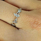 A sterling silver band ring with an integrated leaves design, displayed on a person's finger.