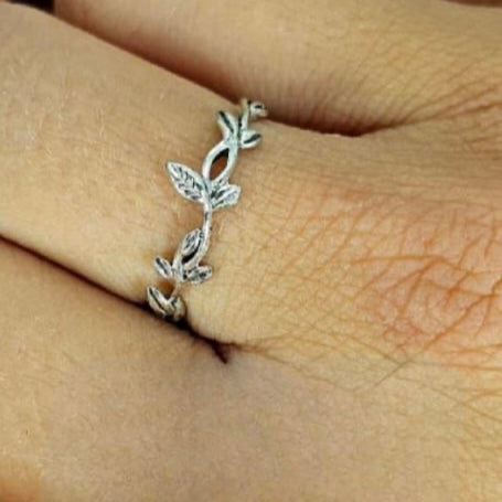 A sterling silver band ring with an integrated leaves design, displayed on a person's finger.
