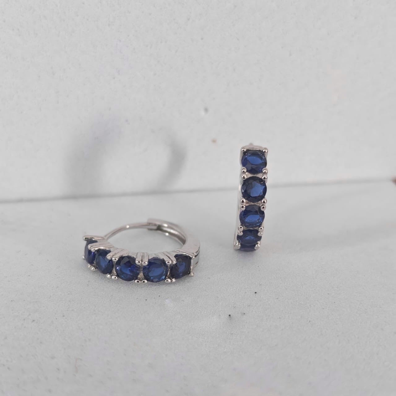 Pair of silver hoop earrings with blue gemstones on a light gray background