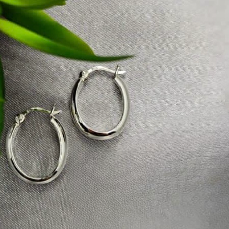 A pair of sterling silver hoop earrings with a clip clasp on a textured grey background.