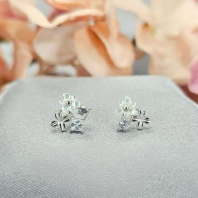 Three flower stud earrings made with sterling silver and adorned with cubic zirconia, displayed on a textured surface with a floral background.