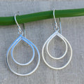 Silver teardrop earrings hanging on a green rod with a gray background