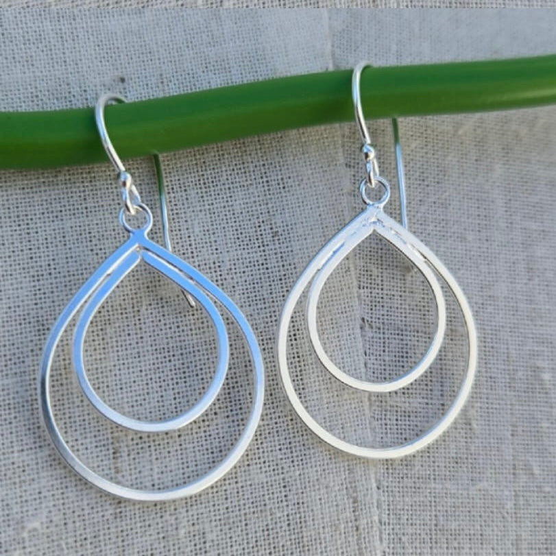 Silver teardrop earrings hanging on a green rod with a gray background