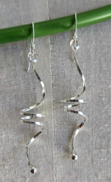 Silver spiral earrings hanging on a green stick against a gray background