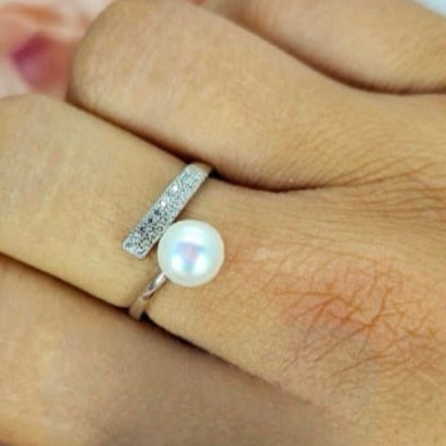 An adjustable sterling silver ring featuring a cubic zirconia bar and a freshwater pearl, displayed on a person's finger.