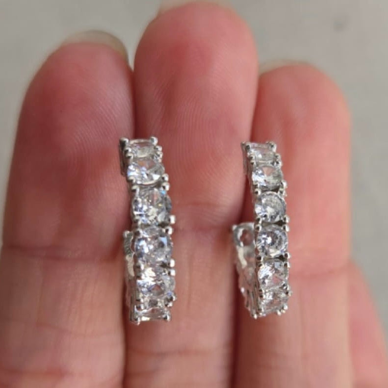 Diamond earrings held between two fingers against a neutral background