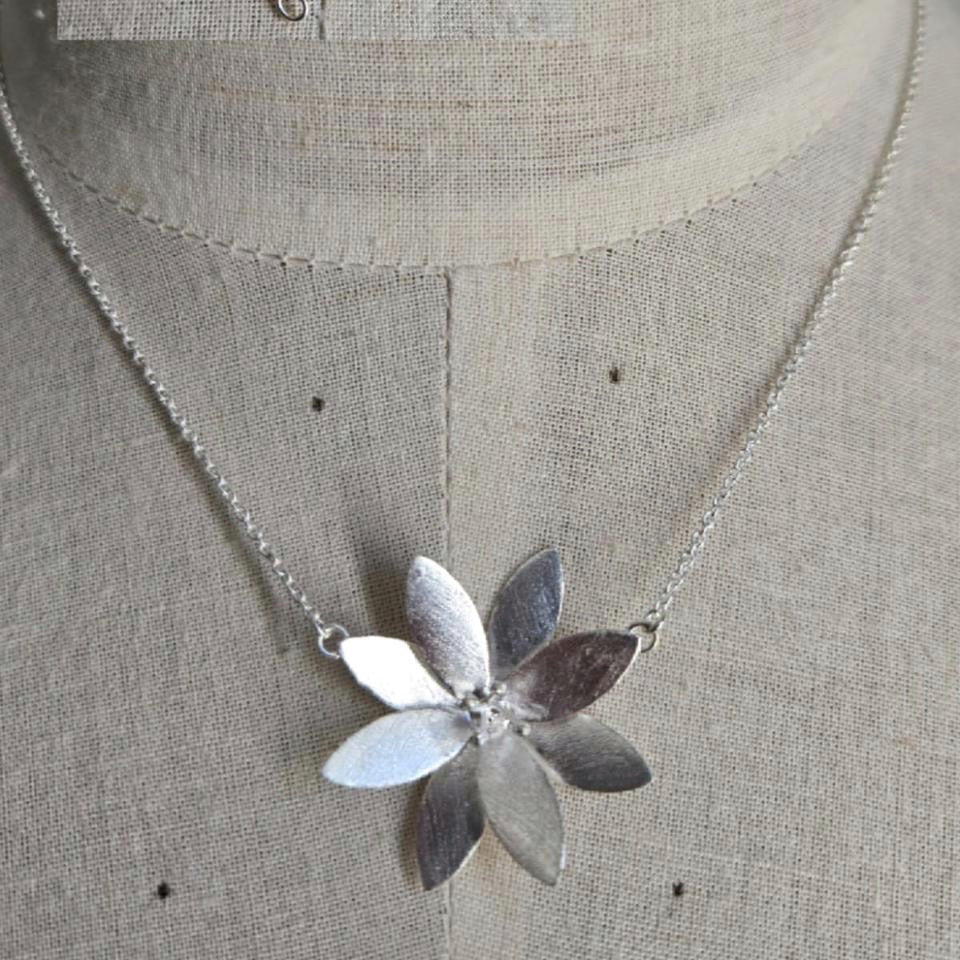 Silver necklace with a flower pendant on a mannequin.