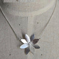 Silver necklace with a flower pendant on a mannequin.