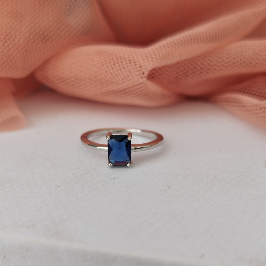 Ring with a blue gemstone on a white surface with pink fabric in the background