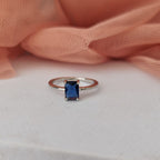 Ring with a blue gemstone on a white surface with pink fabric in the background