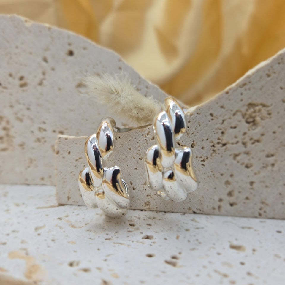 Gold and silver hoop earrings on a textured stone surface with a blurred natural background