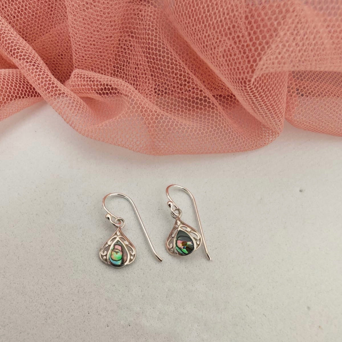 Pair of silver earrings with green gemstones on a white surface with pink fabric in the background
