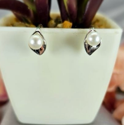 A pair of sterling silver earrings with freshwater pearl centers, displayed in front of a white potted plant.