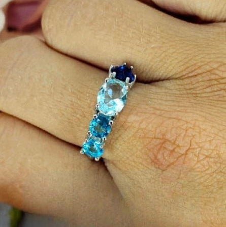 A sterling silver ring with blue cubic zirconia stones worn on a person's finger.