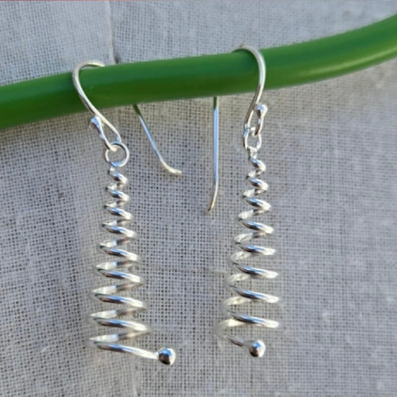 Silver spiral earrings hanging on a green rod against a gray background