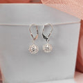 Silver earrings with intricate designs on a light gray box with pink fabric background