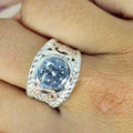 A person's hand displaying a silver filigree ring with a large blue cubic zirconia centerpiece.