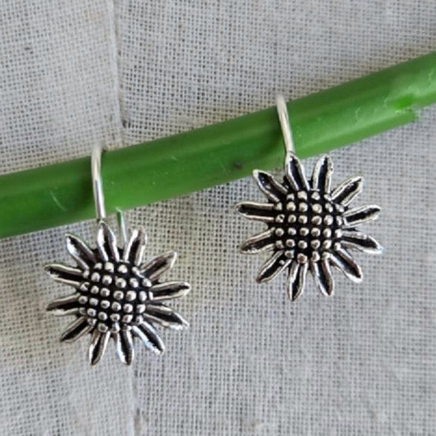 Silver sunflower-shaped earrings on a green stick against a textured fabric background