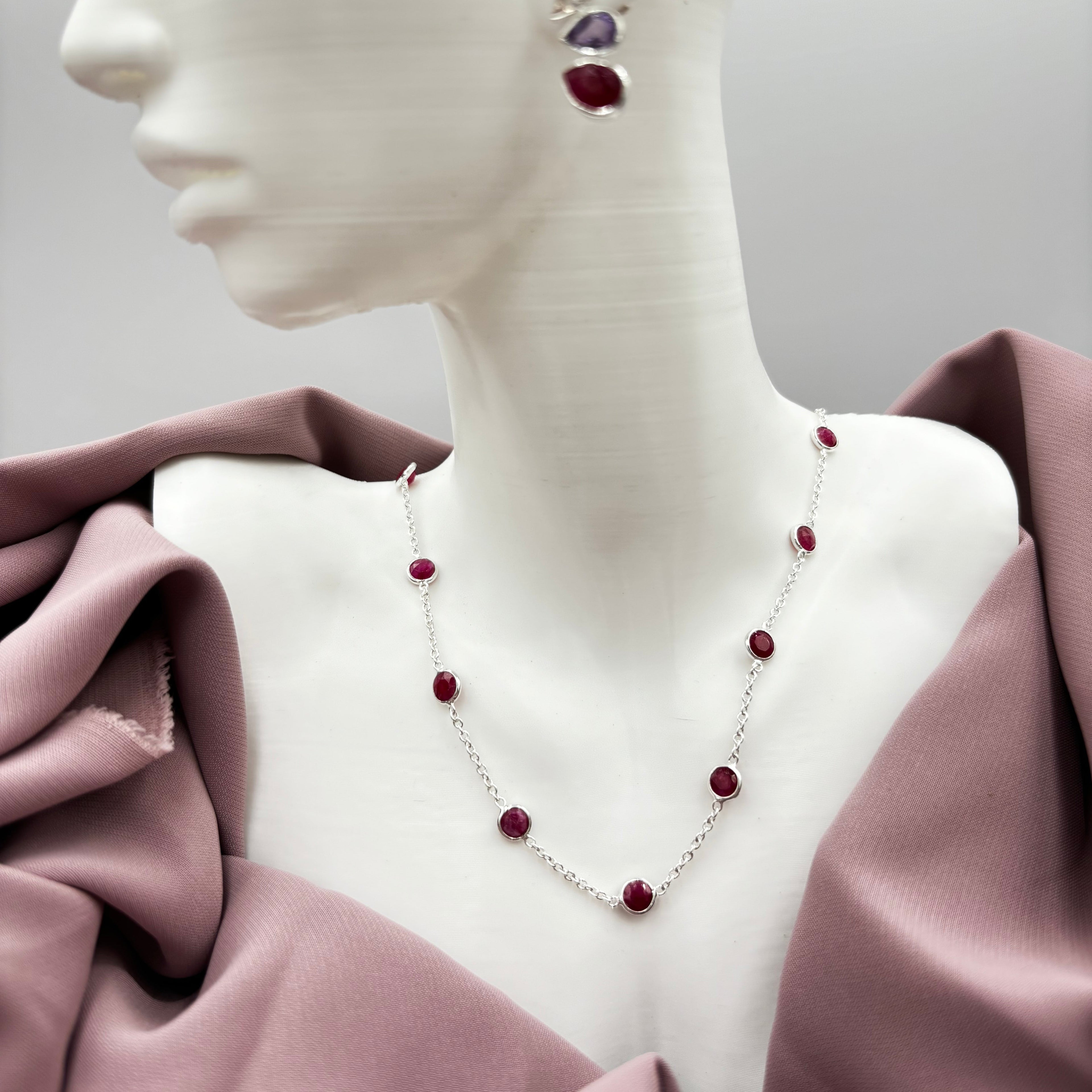 A sterling silver necklace with red ruby semi precious stones displayed on a mannequin.