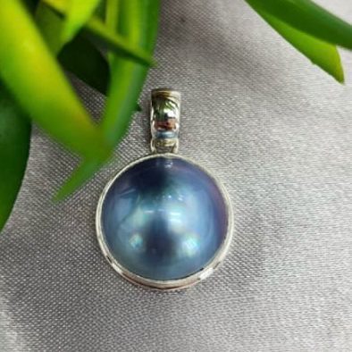 A blue mabe pearl pendant set in sterling silver, displayed against a fabric background.