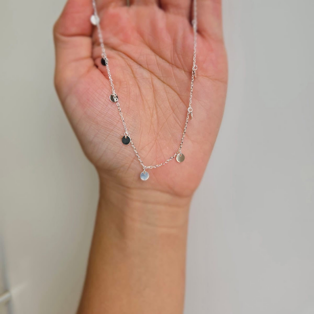 A hand holding a sterling silver necklace with multiple tiny round drops.