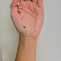 A hand holding a sterling silver necklace with multiple tiny round drops.