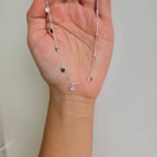 A hand holding a sterling silver necklace with multiple tiny round drops.