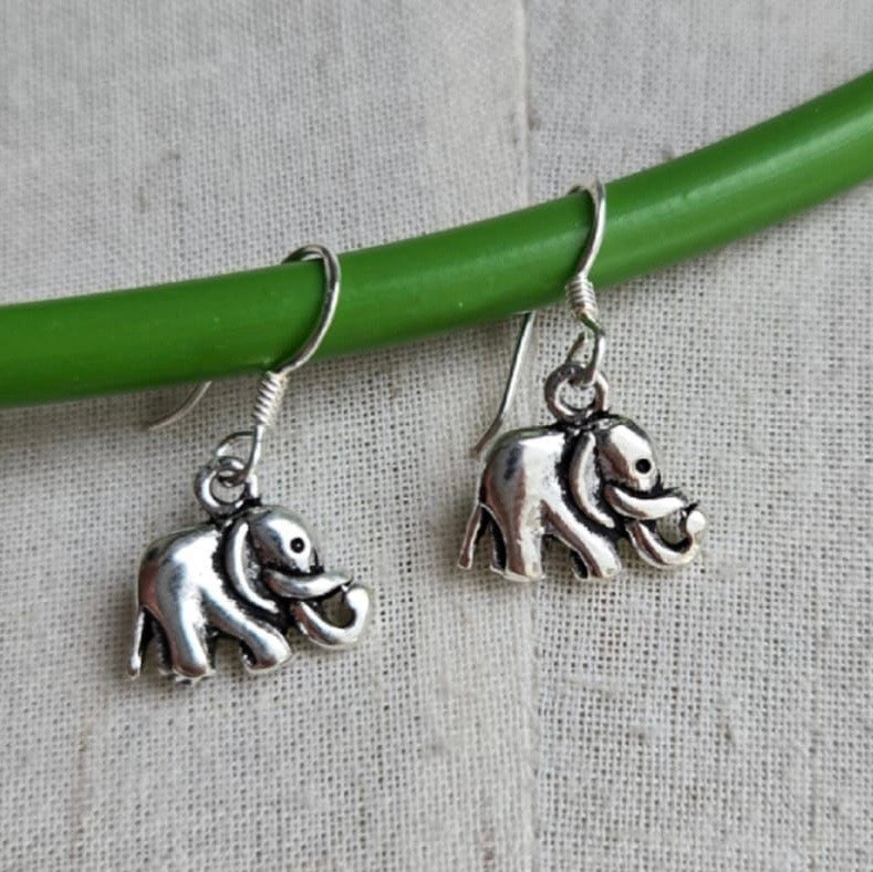 Silver elephant earrings hanging from a green rod on a textured gray background
