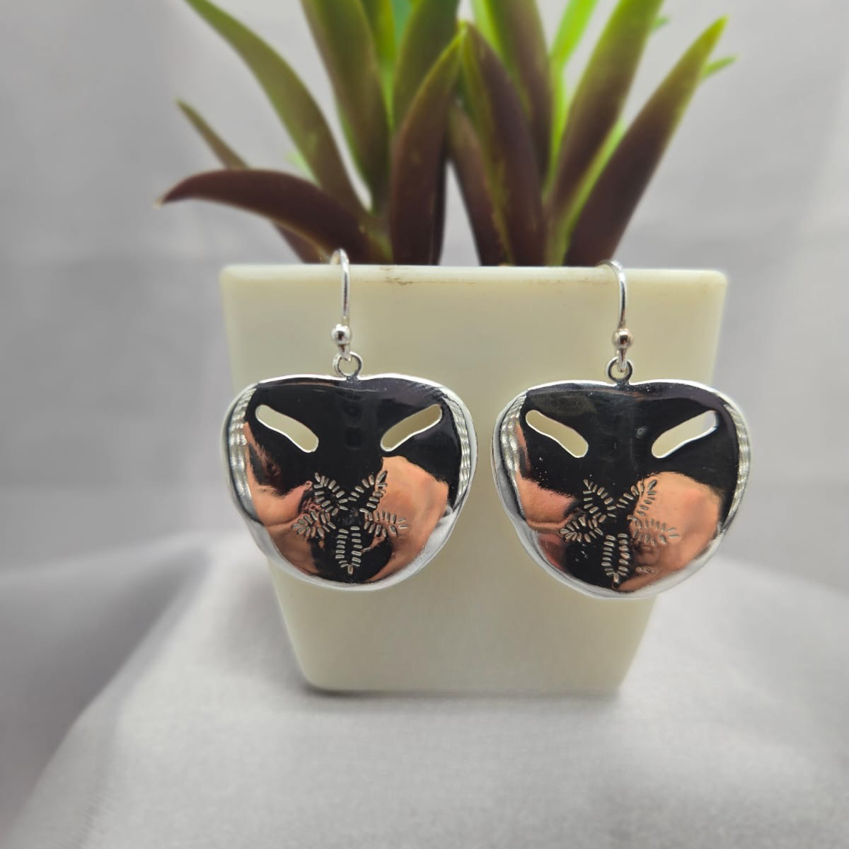 Heart-shaped earrings with black and gold design in front of a potted plant.