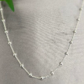 A silver ball chain necklace laid out on a textured surface with a green leaf in the background.