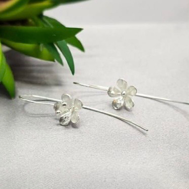 Sterling silver hoop earrings with floral designs, displayed on a white fabric surface.