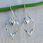 Silver heart-shaped earrings hanging on a green wire against a gray background