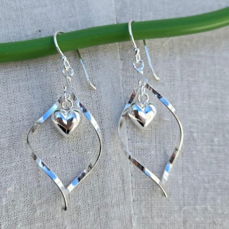 Silver heart-shaped earrings hanging on a green wire against a gray background
