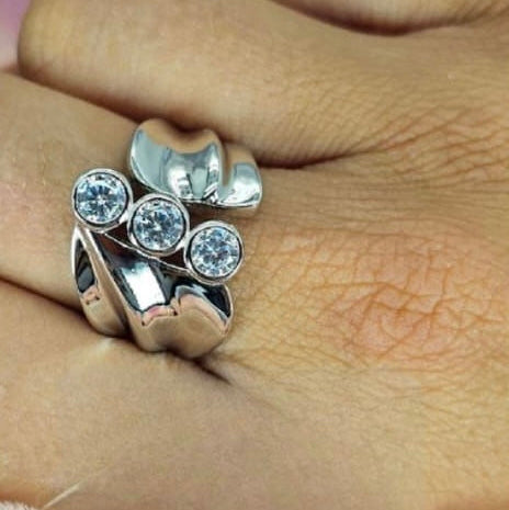 A person's hand wearing a sterling silver ring with three cubic zirconia stones set on the top surface.