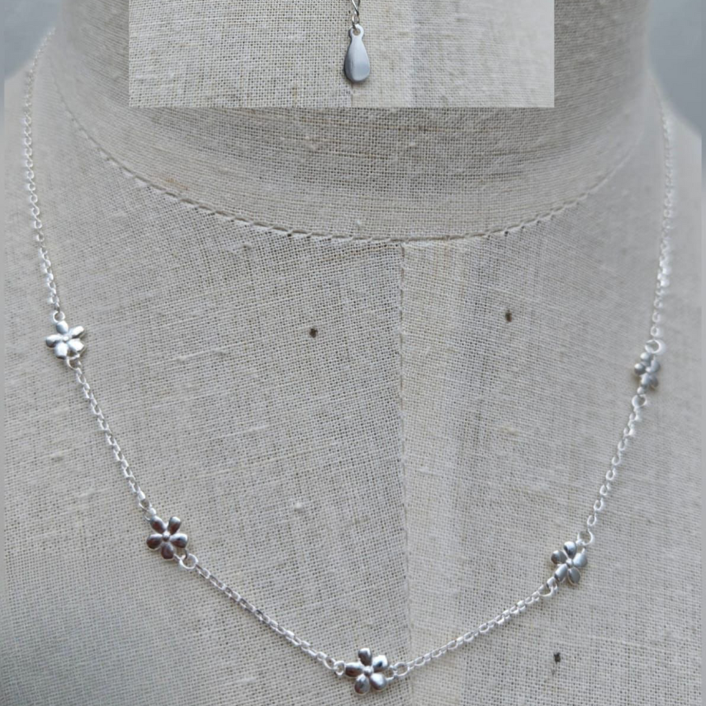 Silver necklace with floral pendants on a mannequin.