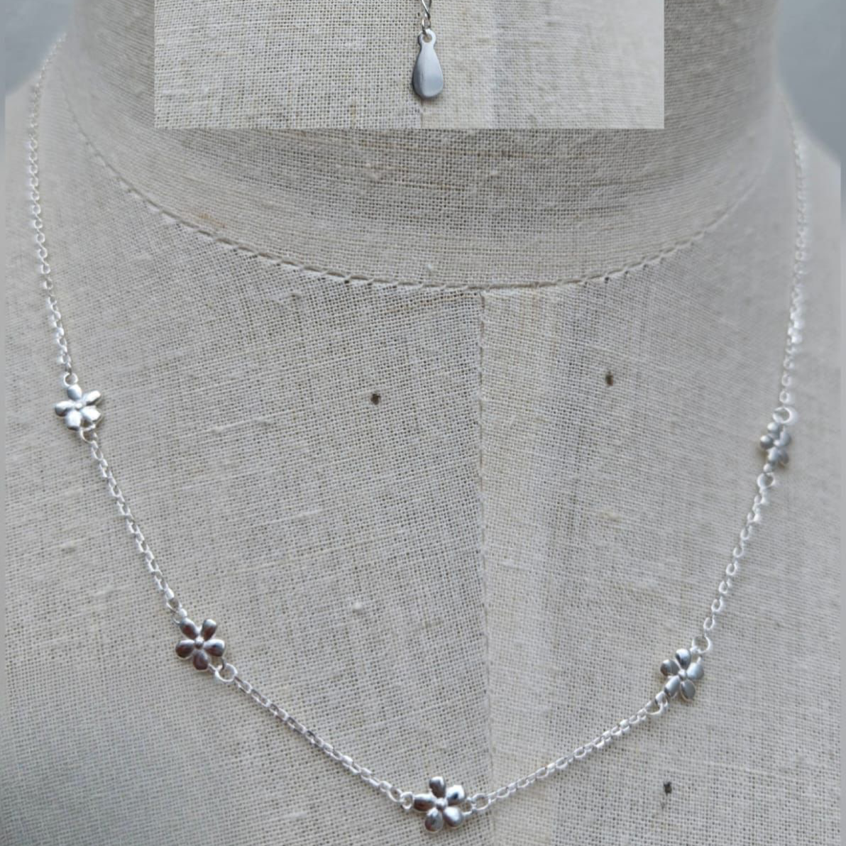 Silver necklace with floral pendants on a mannequin.