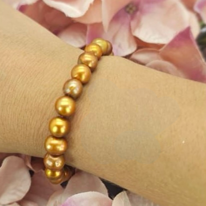 A gold-looking freshwater pearl bracelet on a person's wrist, with pearls ranging from 7-9 mm in size, displayed against a floral background.
