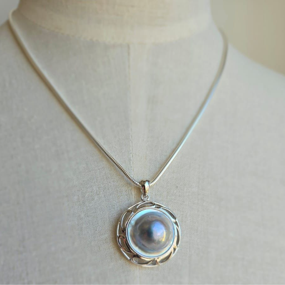 An 18mm grey/blue Blister Mabe pearl pendant set in a sterling silver filigree setting, displayed on a mannequin.