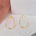 Gold teardrop earrings on a white surface with a pink mesh background