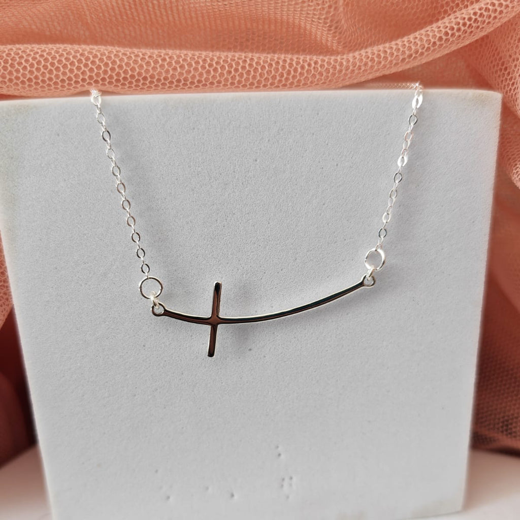 Necklace with a unique design on a white stand against a soft pink background