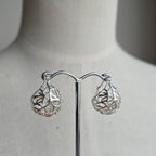 Silver earrings on a mannequin stand with a neutral background
