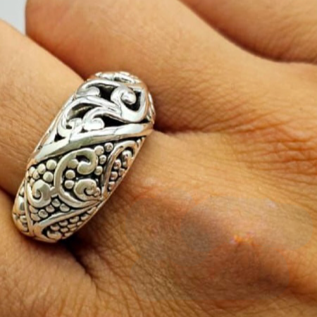 A sterling silver ring with intricate filigree designs, displayed on a person's finger.