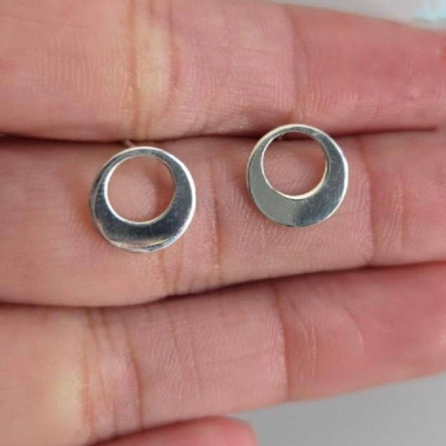 Silver circular earrings held between fingers on a neutral background